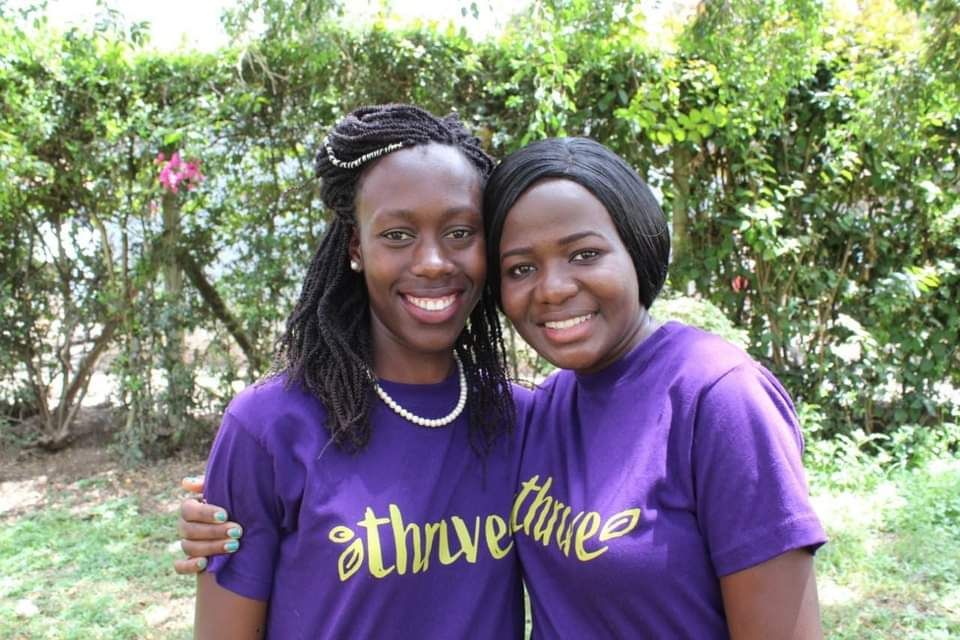 Two women in Kenya hugging and smiling wearing purple t-shirts that say Thrive